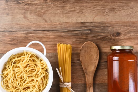 Italian Cooking Still Life with copy space. Woden spoon, dry spaghetti, cooked pasta and a jar of sauce on a wood kitchen table.