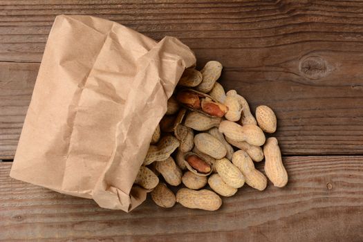 HIgh angle view of peanuts spilling from brown paper bag, Horizontal format on a wood background.