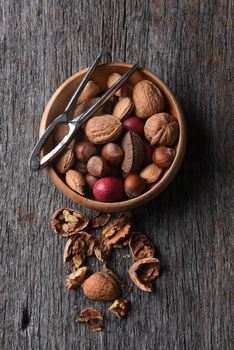 Top view of a bowl of mixed nuts with nutcracker and cracked nuts on a rustic wood table.