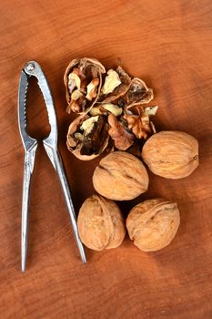 High angle shot of some walnuts and a nutcracker on a wood surface, one nut is cracked in half. Vertical format.