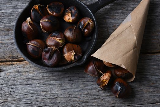 Roasted chestnuts in pan and a paper sack full of cooked nuts.