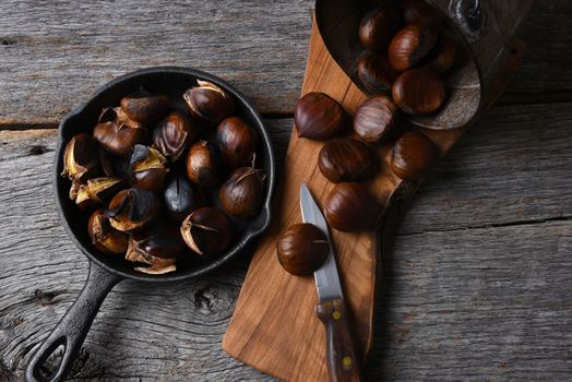 A bucket of fresh chestnuts and a pan full of roasted nuts