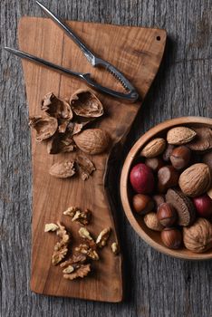 Cracked walnuts and nutcracker on a cutting board with a bowl of mixed whole shelled nuts.