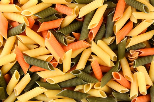 Tri-color penne pasta, filling the frame. Tomato, spinach and wheat pastas are shown, horizontal format.