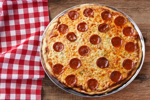 Fresh Homemade Pepperoni Three Cheese Pizza on a red checkered table cloth on a wood table with copy space, horizontal format. 