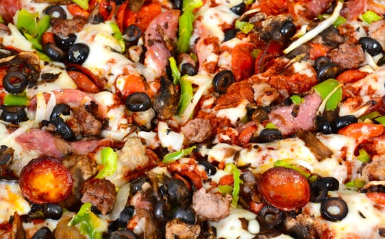 Closeup of a pizza with pepperoni, olive, sausage, onions, peppers, cheese, mushrooms and salami.