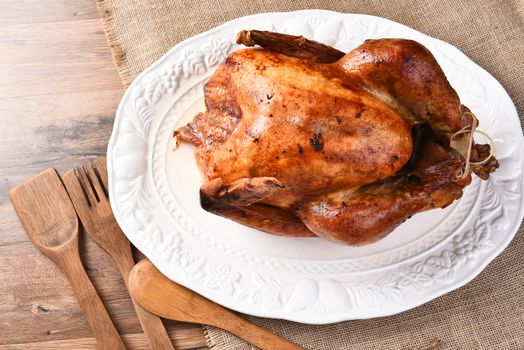 High angle view of a fresh roasted Thanksgiving turkey on a white platter with burlap table cloth and wood utensils.