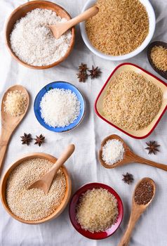 Top view of assorted grains in bowls on a white table cloth.