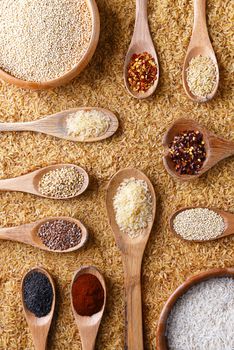 Top view of a bed of brown rice with bowls and spoons with various rices, grains and spices.