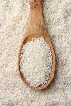High angle closeup shot of a wooden spoon full of uncooked rice grains laying on a bed of grain. Vertical format.