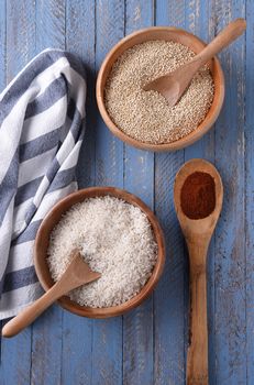 Wood Bowls of Rice and Quinoa on a rustic blue table with a kitchen towel and a spoon of paprika.