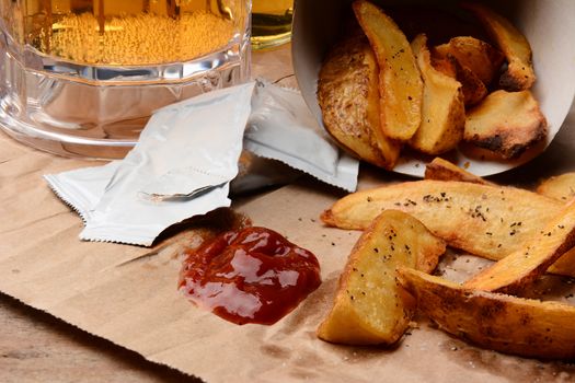 French Fries spilled onto a brown bag. Ketchup dollop and packets  with salt and pepper and mug of beer. Horizontal format filling the frame.