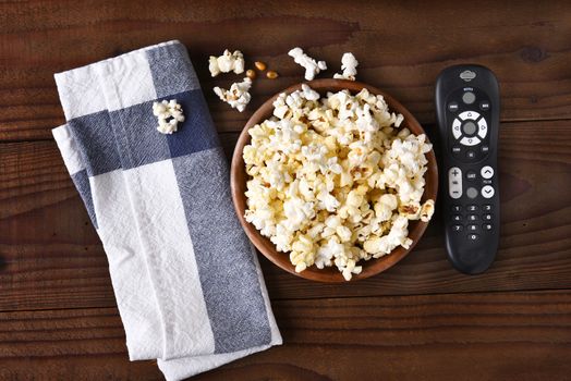 A bowl of popcorn, towel and a TV remote on a rustic wood table 