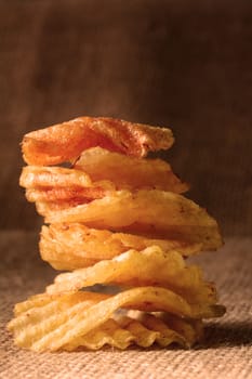 A stack of potato chips with warm side light. Vertical format on a burlap surface.