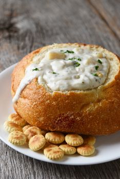 Closeup vertical of New England Style Clam Chowder in a bread bowl, with oyster crackers and copy space.