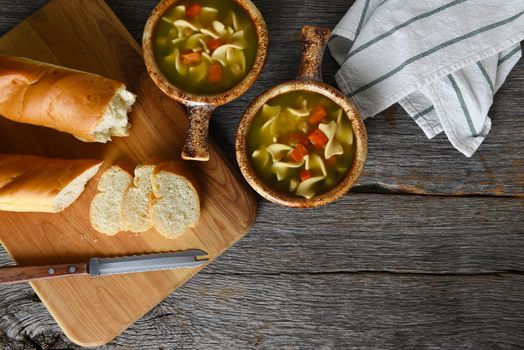 Top view of two bowls of homemade Chicken Noodle Soup with fresh baked loaf of bread. Horizontal with copy space.