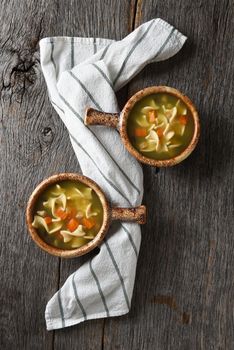 Flat lay with two bowls of homemade Chicken Noodle Soup on a rustic wood table with a kitchen towel.