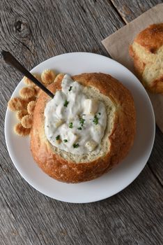 Overhead view of a bread bowl of New England Style Clam Chowder on a rustic wood table. 