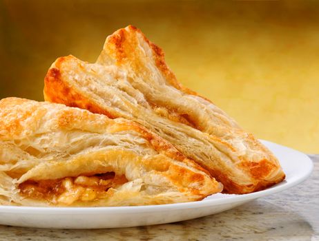 Closeup of two apple turnovers on a plate and granite counter top with warm mottled background.