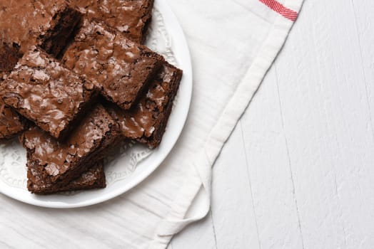 Flat lay view of a plate of fresh homemade brownies on a white plate, towel and wood kithcen table.