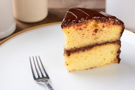 A slice of yellow cake with chocolate frosting on a white plate with a fork.