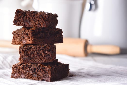 Closeup of a plate of fresh homemade brownies on a white towel and wood kithcen table, with canisters and rolling pin in the background.