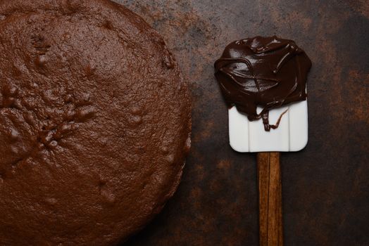 Flat lay closeup of a unfrosted chocolate cake with a spatula and a glob of icing.