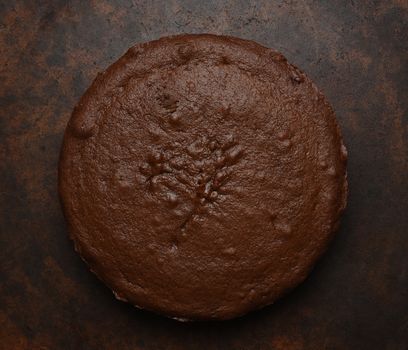 Flat lay of a single layer chocolate cake on a dark brown mottled background. 