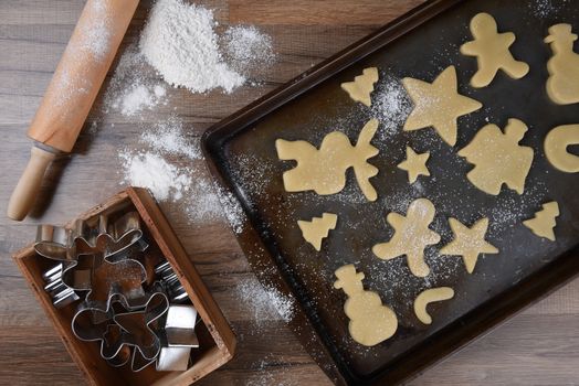 Top view of a baking sheet with a holiday shaped sugar cookies, with a rolling pin and wood box of cookie cutters on the side.
