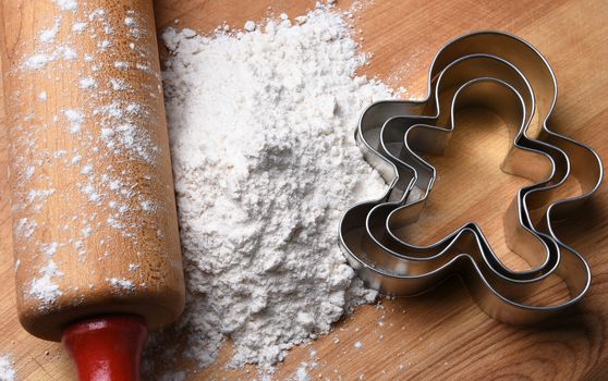 Closeup top view of a rolling pin on a cutting board with flour and gingerbread man cookie cutters. 