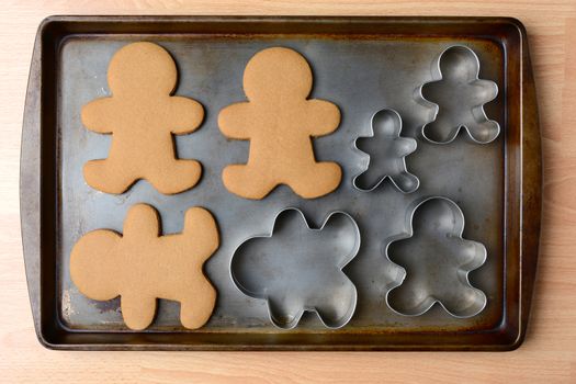 High angle shot of an old baking sheet with holiday gingerbread man cookies and cookie cutters. Horizontal format on wood kitchen table.