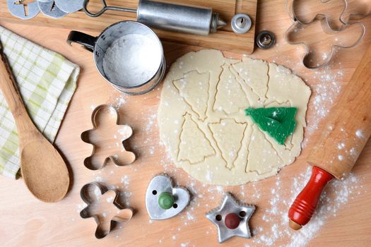 Baking holiday cookies still life shot form a high angle. Horizontal format with cookie dough, cutters, sifter, flour, rolling pin, cookie press, spoon, towel on butcher block surface.