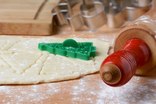 Closeup Christmas baking still life with rolling pin, cookie dough, cutters and flour on a wood butcher block surface.