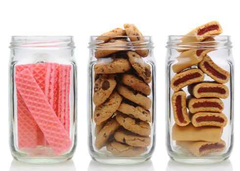 Three glass jars filled with cookies, on a white background with reflection. Jars contain, pink sugar wafers, chocolate chip and fruit bars.