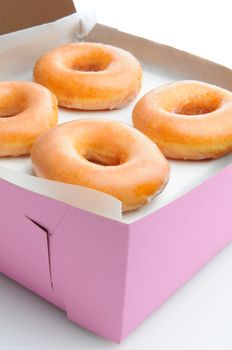 Closeup of four glazed donuts in a pink bakery box. Vertical format with a white background.