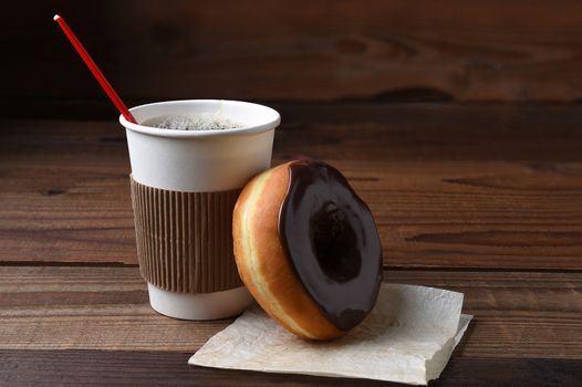 A chocolate frosted donut leaning on a hot cup of fresh brewed coffee. 