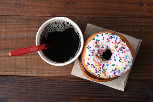 High angle view of a paper cup of hot fresh brewed coffee next to a stack of fancy donuts.