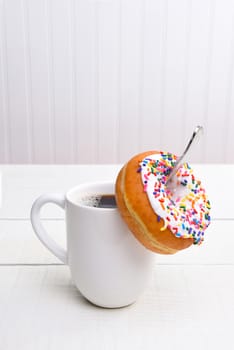 Closeup of a mug of hot coffee with a donut hanging off the spoon inside the cup. Vertical with copy space.
