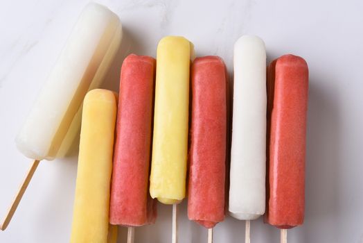 Top view of a group of assorted ice pops on a marble counter top. Red, yellow and white fruit flavored pops on their sides.