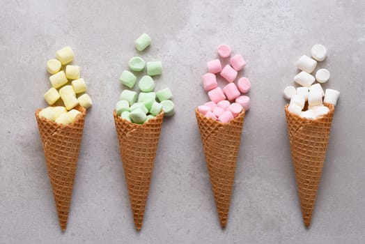 Four Sugar Waffle Ice Cream Cones filled with colorful marshmallows spilling onto tile table. 