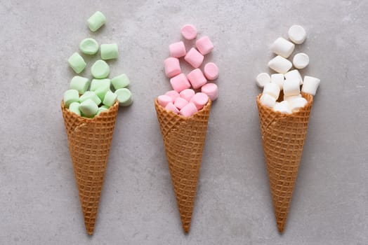 Closeup of three Sugar Waffle Ice Cream Cones filled with colorful marshmallows spilling onto tile table. 