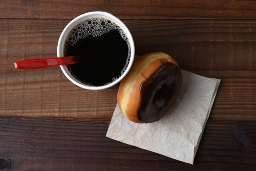 High angle shot of a chocolate frosted donut leaning on a hot cup of fresh brewed coffee. 