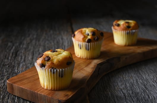 Closeup of three mini chocolate chip muffins on a cutting board. Horizontal format with copy space.