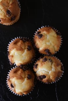 Top closeup view of a group of mini chocolate chip muffins on black slate. Vertical format. 