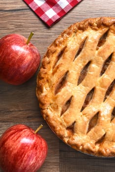 High angle closeup view of a fresh baked apple pie with apples on a rustic wood table. Vertical format.