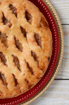 High angle closeup of an fresh baked lattice crust apple pie on holiday chargers. The dessert is on red and gold chargers on a white wood table. Vertical format.