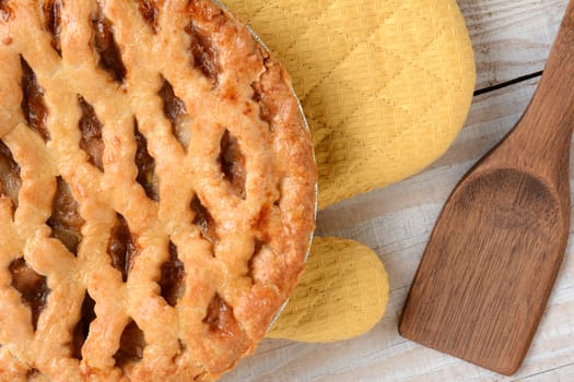 High angle shot of a fresh baked apple pie with lattice crust on an oven mitt. Horizontal format on a rustic white wood kitchen table.