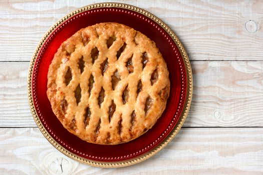 High angle shot of a fresh baked apple pie on stacked red and gold chargers. Horizontal format on a rustic white table with copy space.