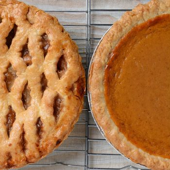 Closeup of holiday Apple and Pumpkin Pies on cooling racks. Only half of each pie is shown. Square format.