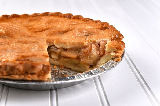 Closeup of a fresh baked apple pie with a slice missing. Shallow depth of field on a white bead board background.